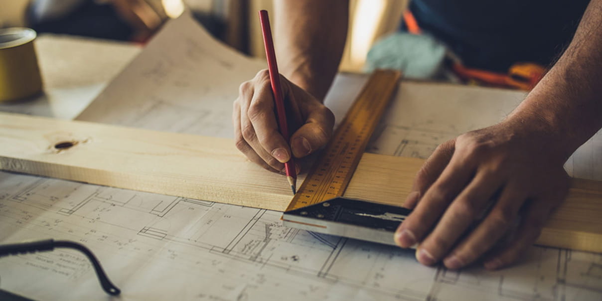 木材の上に定規を当てて鉛筆で線を引いている作業中の手元の様子