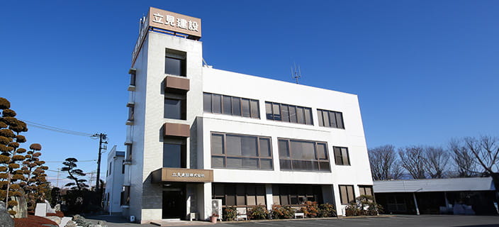 青空の下に建つ白い4階建ての立見建設のビルが正面から写っている様子