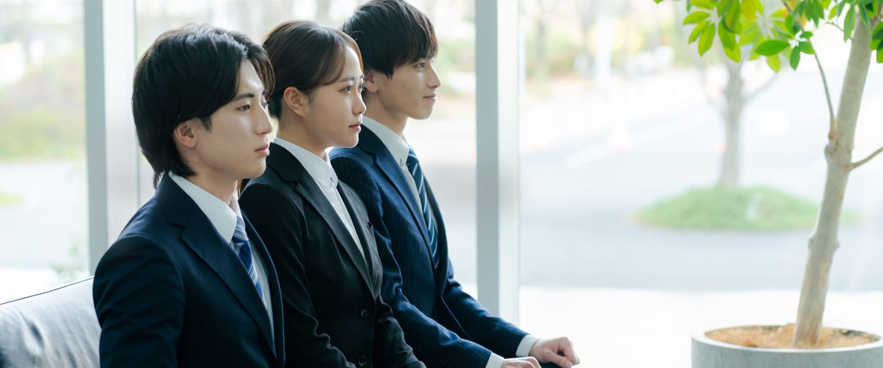 スーツ姿で並んで話を聞いている３人の男性と女性