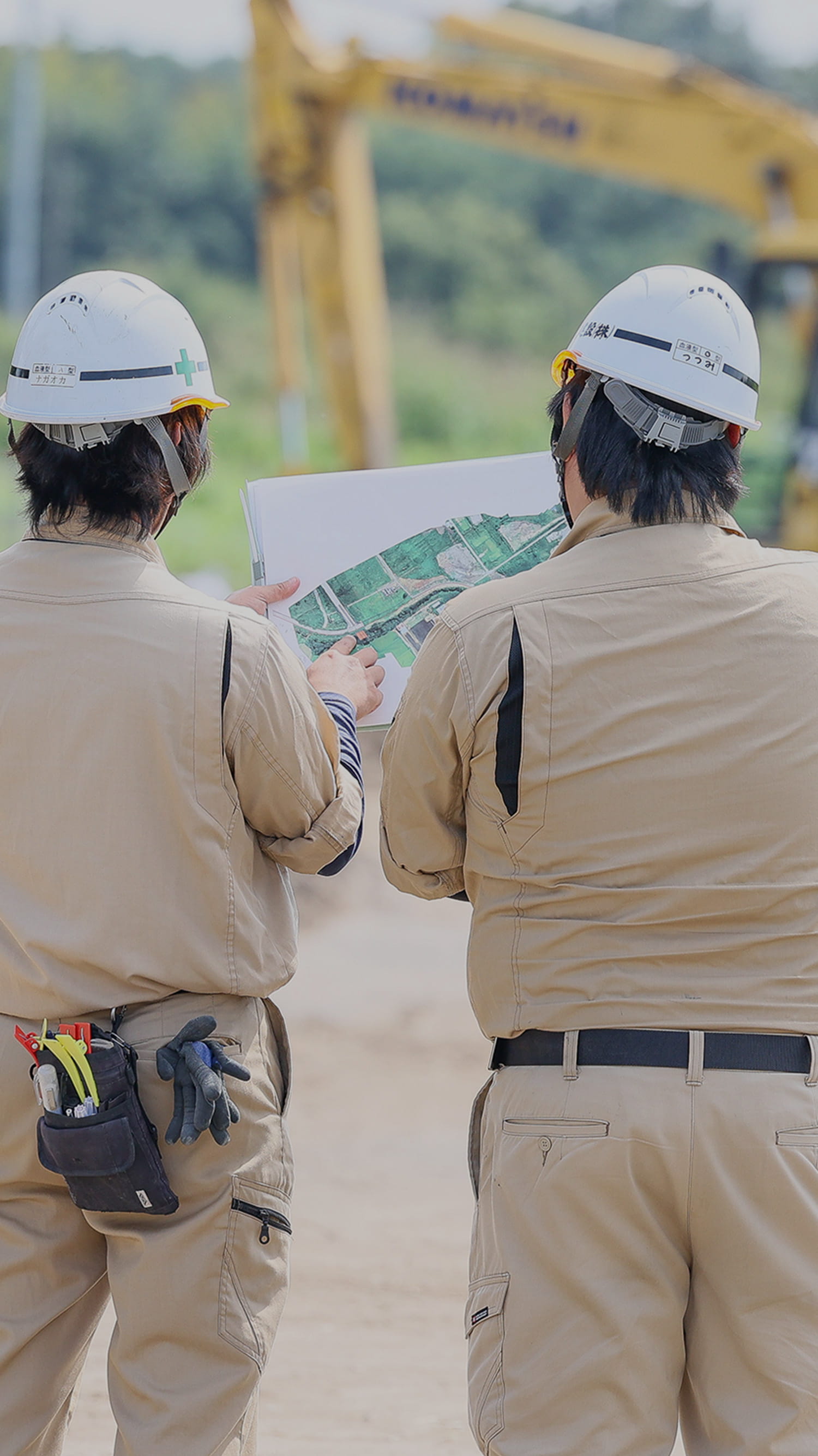 建設現場で図面を見ながら打ち合わせをする二人の作業員の写真