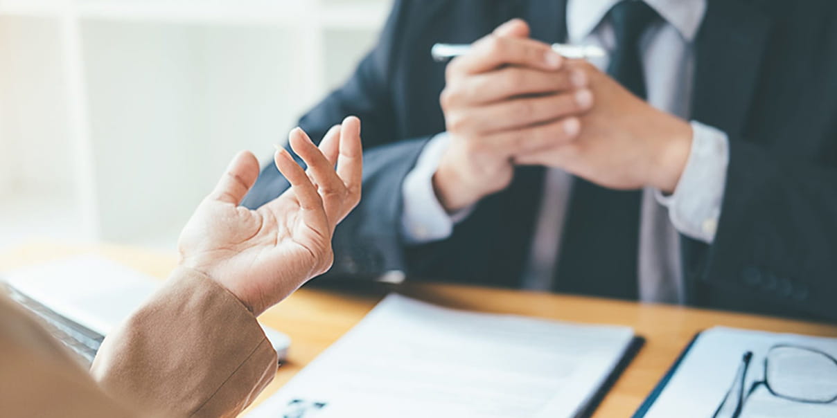 一方が説明するジェスチャーをし、もう一方がペンを持って話を聞いている場面