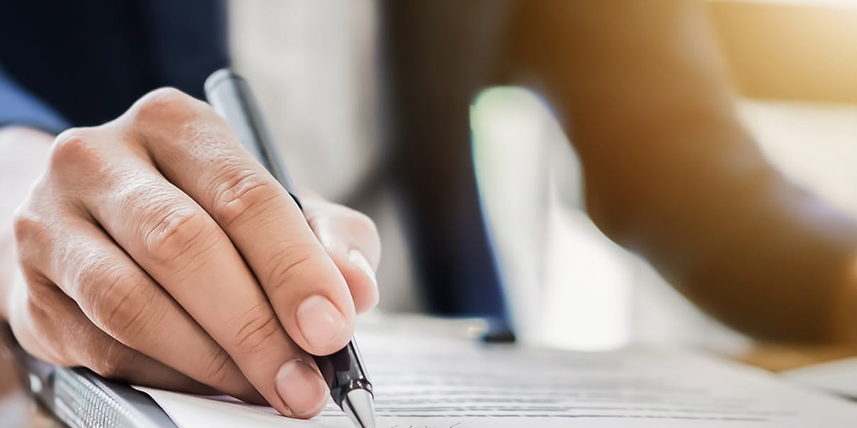 ペンを持った手元が書類に記入している様子のクローズアップ写真